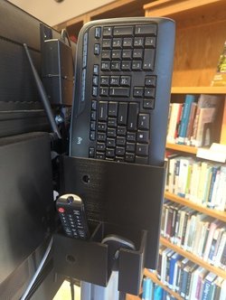 Image of keyboard, mouse, and TV remote in a caddy on the back of a TV cart.